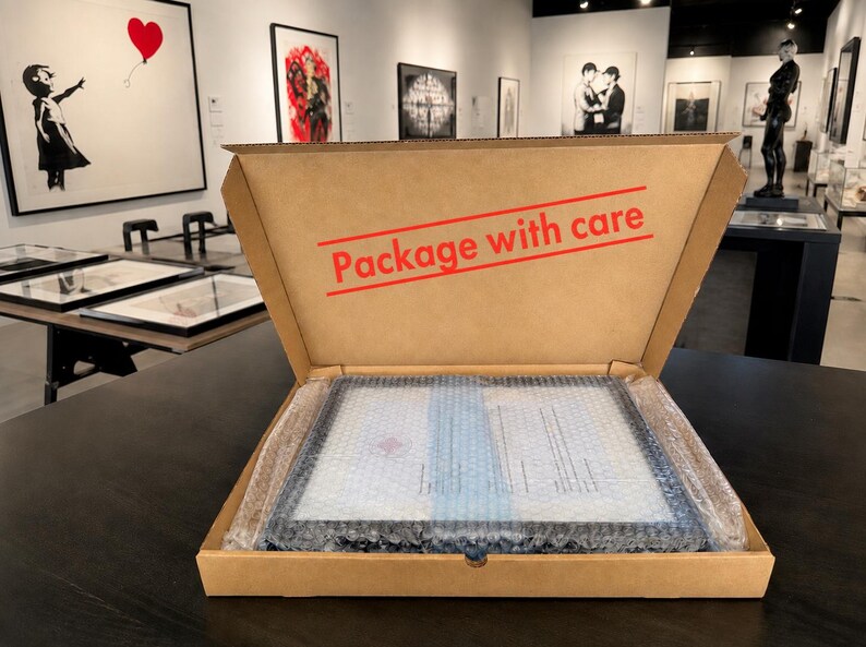 Puede incluir: Una caja de env&iacute;o de cart&oacute;n marr&oacute;n con el texto "Package with care" impreso en rojo en la tapa interior. Dentro de la caja, un objeto rectangular est&aacute; envuelto en pl&aacute;stico de burbujas transparente para proteger el contenido durante el transporte.