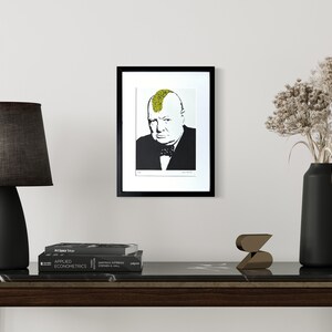 May include: A framed wall art print featuring a black and white portrait of Winston Churchill with a bright yellow mohawk hairstyle. The portrait is centered within a white mat and a thin black frame, displayed on a plain light-colored wall.