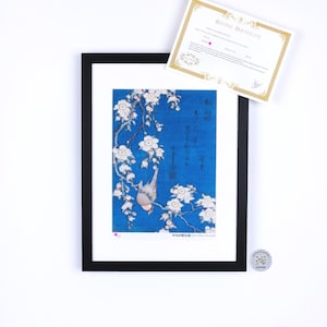 May include: Framed art print featuring a blue background with white floral branches and a bird. The artwork is in a black frame, accompanied by a certificate. The print has Japanese text.