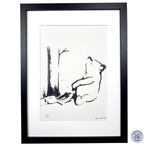 May include: A framed black and white print featuring a stylized bear sitting next to a tree. The artwork includes a small pink circular stamp with the number 160 and a signature in the bottom right corner, all encased in a black frame.