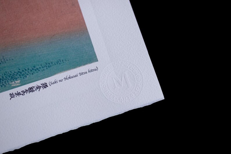 May include: A corner of a print with a landscape scene in shades of blue, green, and orange. The print has Japanese text and a circular embossed seal with the letter "M". The paper has a textured surface.