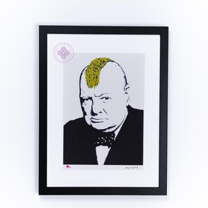 May include: A framed print featuring a black and white portrait of Winston Churchill with a bright yellow mohawk hairstyle. The figure wears a dark suit and a polka dot bow tie. A circular purple logo and a small pink dot appear on the white border.