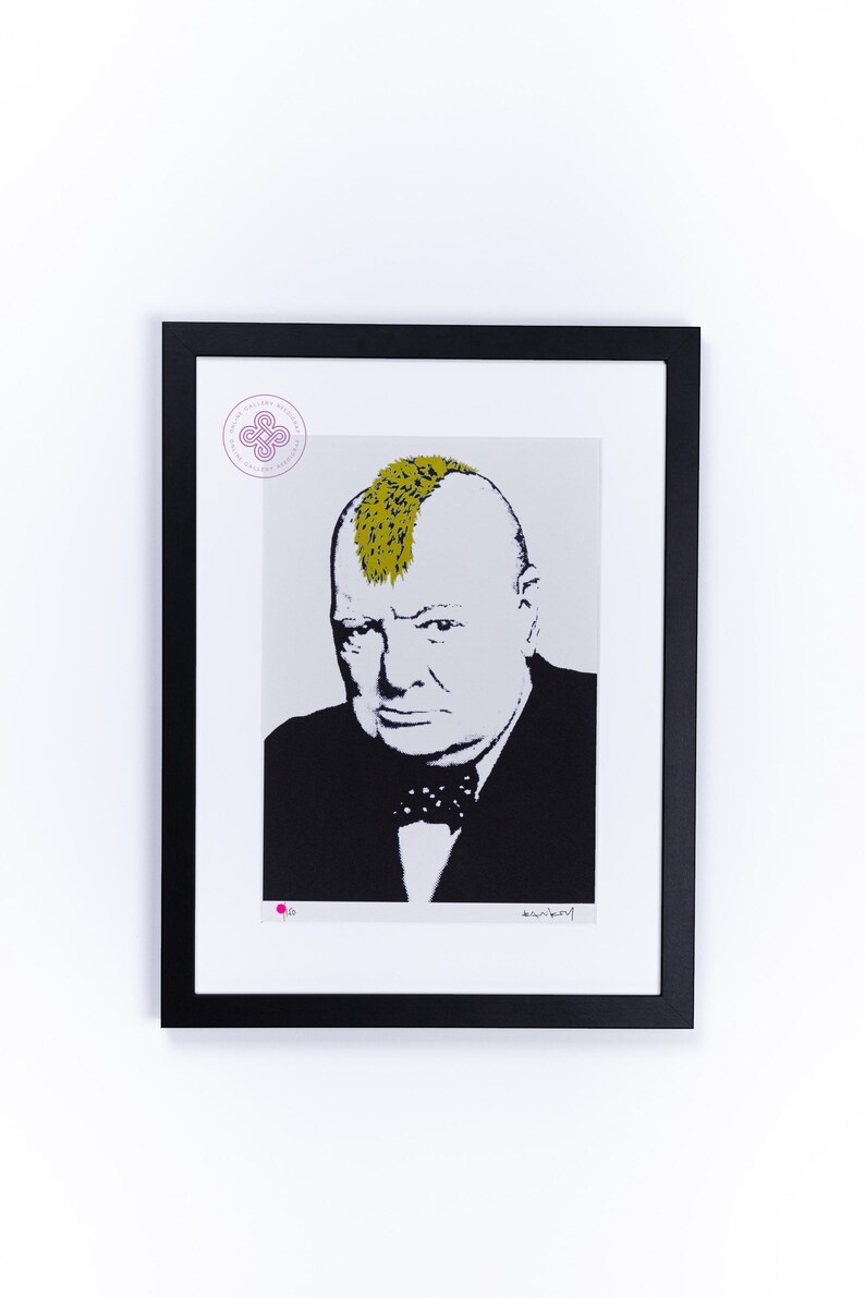 May include: A framed print featuring a black and white portrait of Winston Churchill with a bright yellow mohawk hairstyle. The figure wears a dark suit and a polka dot bow tie. A circular purple logo and a small pink dot appear on the white border.