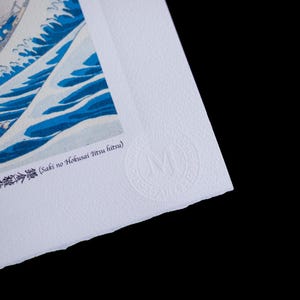 K&ouml;nnte beinhalten: Ein Druck eines japanischen Holzschnittkunstwerks mit einer gro&szlig;en Meereswelle in Blau und Wei&szlig;. Der Druck enth&auml;lt japanischen Text und ein kreisf&ouml;rmiges gepr&auml;gtes Logo. Das Papier hat eine strukturierte Oberfl&auml;che und einen B&uuml;ttenrand.