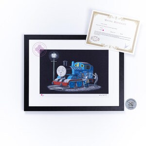 May include: A framed art print featuring a blue steam locomotive with graffiti, illuminated by a street lamp at night. Two figures stand beside the train. The print includes a white mat, a black frame, and an accompanying editing certificate document.