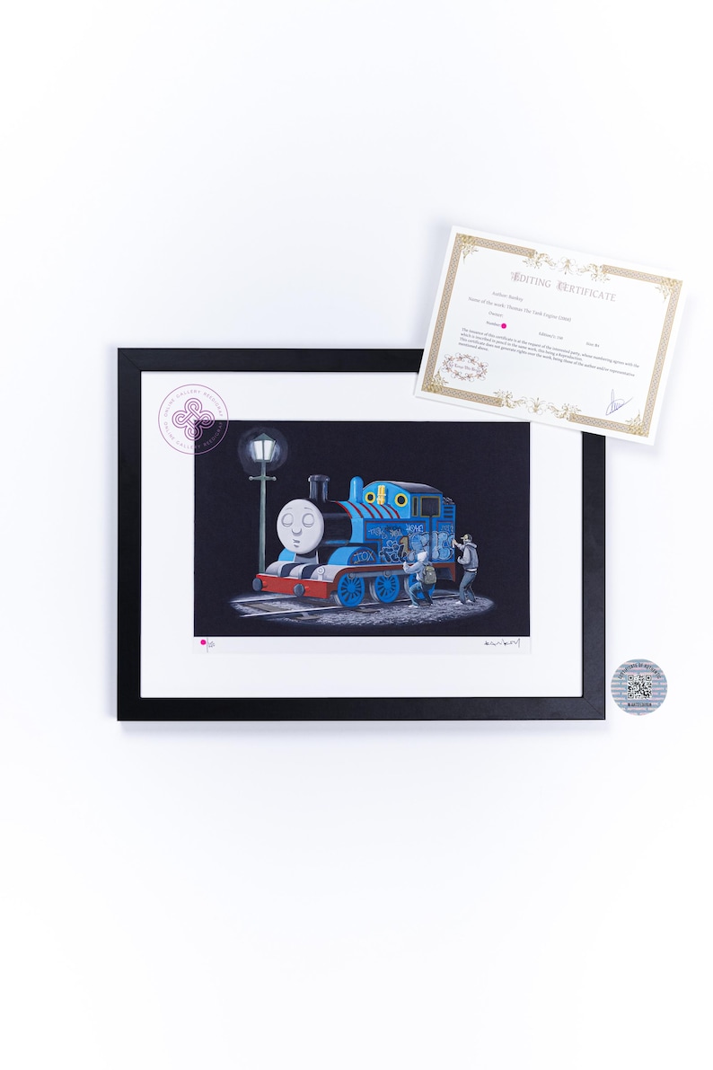 May include: A framed art print featuring a blue steam locomotive with graffiti, illuminated by a street lamp at night. Two figures stand beside the train. The print includes a white mat, a black frame, and an accompanying editing certificate document.