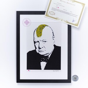 May include: A framed print featuring a stylized black and white portrait of Winston Churchill with a gold mohawk hairstyle. The artwork includes a circular stamp, a signature, and a separate rectangular certificate of authenticity with gold borders.