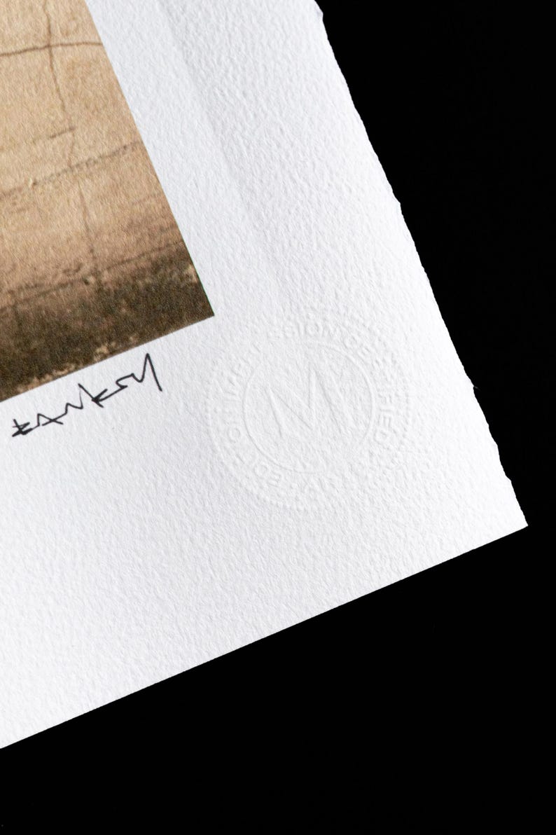 May include: A white paper print with a black signature and a white embossed circle with the letter "M" inside. The circle has the text "Original Limited Edition" around the outside.