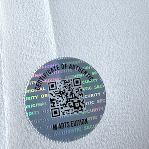 May include: A silver holographic sticker with the text "Certificate of Authenticity" and a QR code. The text "M'Arts Edition" is also visible on the sticker.