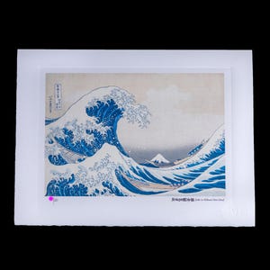 K&ouml;nnte beinhalten: Ein gerahmter Druck von Hokusais "Die gro&szlig;e Welle vor Kanagawa". Das Kunstwerk zeigt eine gro&szlig;e Meereswelle mit einem Berg im Hintergrund. Die Welle ist tiefblau mit wei&szlig;em Schaum. Der Druck befindet sich auf wei&szlig;em Hintergrund.