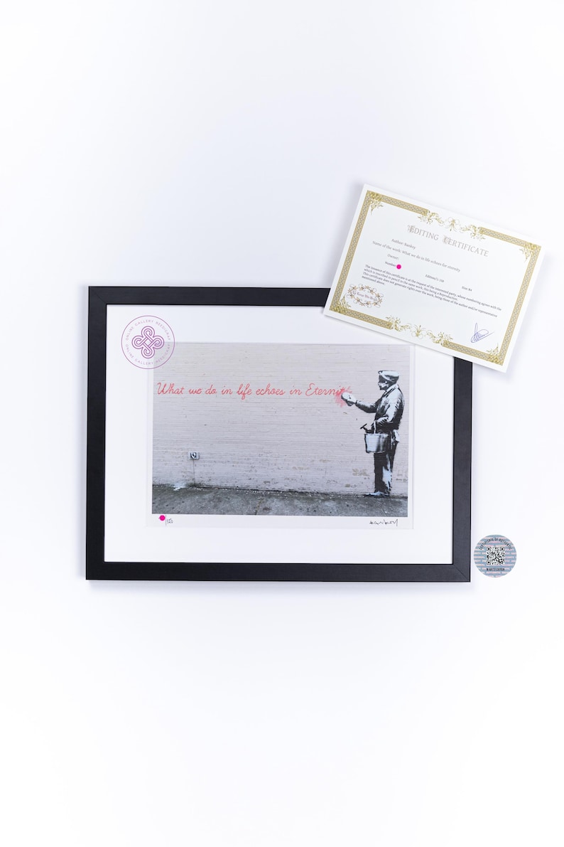Puede incluir: Una impresi&oacute;n enmarcada en blanco y negro que muestra a una persona pintando el texto rojo What we do in life echoes in Eternity en una pared. La impresi&oacute;n incluye un logotipo circular, una firma y un certificado de edici&oacute;n blanco con bordes dorados.