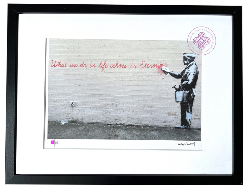 Puede incluir: Una impresi&oacute;n enmarcada que presenta una imagen en blanco y negro estilo plantilla de una persona sosteniendo un cubo y pintando el texto rojo "What we do in life echoes in Eternity" en una pared de ladrillo. Incluye firma y un cuadrado rosa.