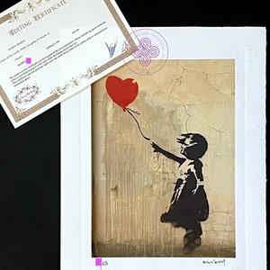 May include: A black and white stencil print of a girl holding a red heart-shaped balloon. The background is a textured, beige wall. The print is signed "Banksy" in the bottom right corner and numbered "250" in the bottom left corner.