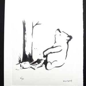 May include: A black and white ink illustration on textured paper depicting a bear sitting next to a tree with a honey pot marked with a dollar sign. The print features the handwritten text 10/150 and a signature, with small red paint splatters.