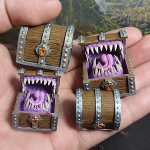 May include: Four miniature treasure chests with a silver and gold finish. Each chest has a different design, including a closed chest, a chest with a toothy mouth, and a chest with a toothy mouth and a pink tongue.