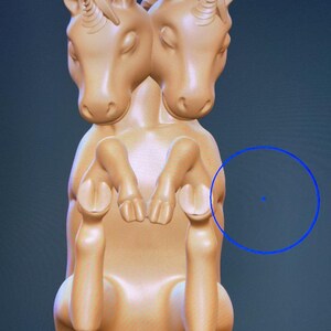 May include: A two-headed unicorn figurine with a light brown color. The figurine is sitting with its legs crossed and its tail curled up.