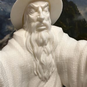 以下が含まれることがあります： 白い3Dプリントされた男性の置物。長い白いひげとつば広の帽子をかぶっています。置物は細部まで作り込まれており、リアルで、表面はテクスチャ加工されています。
