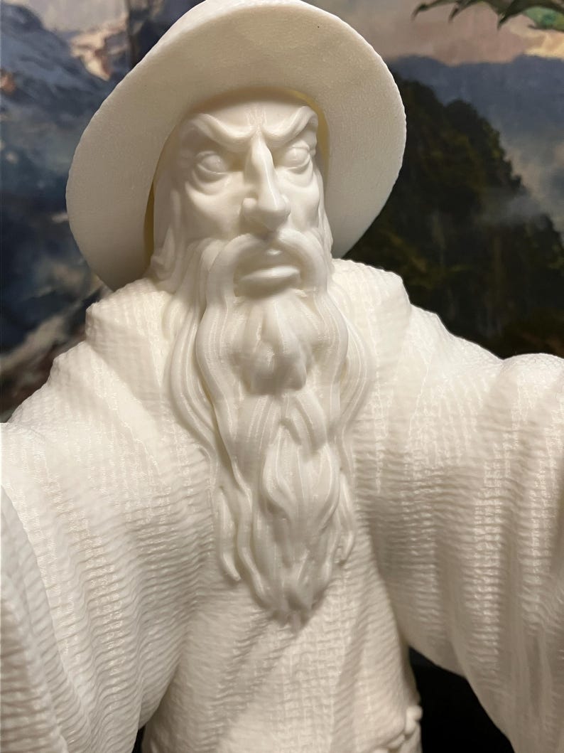 以下が含まれることがあります： 白い3Dプリントされた男性の置物。長い白いひげとつば広の帽子をかぶっています。置物は細部まで作り込まれており、リアルで、表面はテクスチャ加工されています。