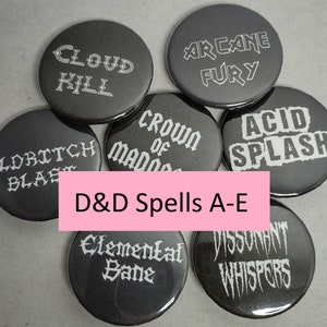 May include: Six black and white button pins with a gothic font design. The pins feature the names of Dungeons and Dragons spells: Cloud Kill, Arcane Fury, Acid Splash, Crown of Madness, Eldritch Blast, and Dissonant Whispers.