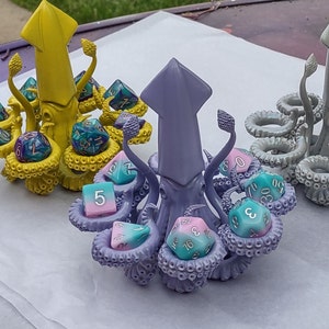 May include: Purple and pink 3D printed squid dice tower with eight dice, including a pink and blue die with the number 5, a pink and blue die with the number 3, a pink and blue die with the number 16, a green and blue die with the number 70, a green and blue die with the number 8, a green and blue die with the number 6, a green and blue die with the number 2, and a green and blue die with the number 0.