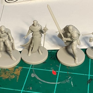 May include: Four gray plastic miniature figurines of fantasy characters, each standing on a round base. The characters include a warrior with a sword, a wizard with a staff, a cleric with a mace, and a dwarf with an axe.