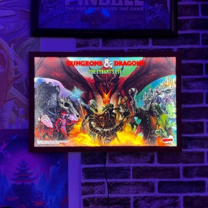 May include: A red, white, and black framed light-up sign with the words "Dungeons & Dragons The Tyrant's Eye" in white text. The sign features a fantasy illustration of a dragon, knights, and a wizard.