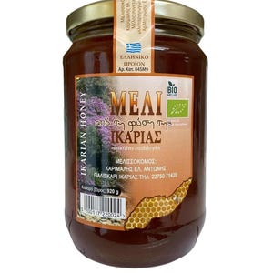 May include: A glass jar of Ikarian honey with a gold lid. The label features Greek text, a honeycomb illustration, and the words "IKARIAN HONEY." The jar contains a golden-brown liquid, and the net weight is 920 grams.