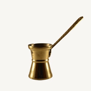 May include: A gold-colored metal coffee pot with a long handle. The pot has a rounded base and a narrow neck.
