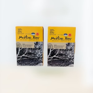 May include: Two boxes of Chios Gum Mastic, a natural resin, with a yellow background and a black and white image of a tree branch. The boxes are labeled "Mastiha Chiou" and "Chios Gum Mastic".