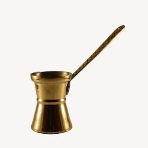 May include: A gold-colored metal coffee pot with a long handle. The pot has a rounded base and a narrow neck.