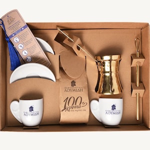 May include: A brown cardboard box with a gold coffee pot, two white coffee cups, and a blue tassel bookmark. The box has the text "Καφεκοπτεία ΛΟΥΜΙΔΗ 100 χρόνια στις καρδιές σας" printed on it.