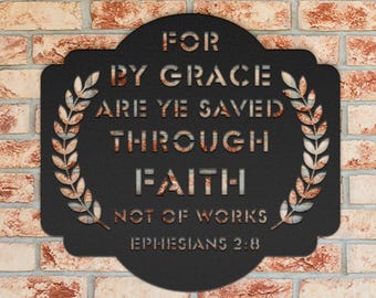 May include: Black metal wall art with the text "FOR BY GRACE ARE YE SAVED THROUGH FAITH NOT OF WORKS EPHESIANS 2:8". The sign has a decorative border of wheat stalks and is mounted on a brick wall.