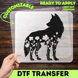 May include: A clear DTF transfer sheet featuring a black silhouette of a wolf with a floral pattern integrated into its body. The design includes text that reads CUSTOMIZABLE, READY TO APPLY, NEXT DAY SHIPPING, and DTF TRANSFER.