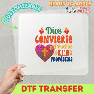 May include: A DTF transfer with the text "Dios Convierte Pruebas En Propósitos" in orange, green, and blue. A heart-shaped floral design with a cross is in the center. The words "Customizable" and "Ready to Apply" are also visible.