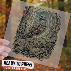 May include: A DTF transfer sheet featuring a detailed illustration of a raven perched on a mossy log within a forest setting. The text RAVEN WISDOM is printed on the log. The design includes intricate line work in shades of black, green, and brown.