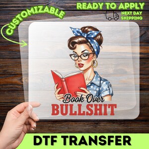 May include: A DTF transfer sheet featuring a retro-style illustration of a person with brown hair wearing a blue polka dot headscarf and glasses, reading a red book. The text below reads Book Over BULLSHIT in black and red lettering.