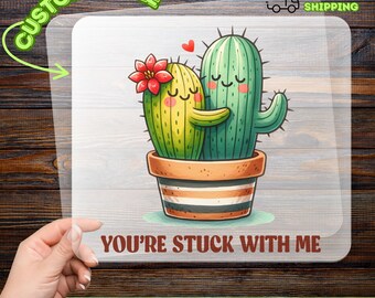 May include: A DTF transfer featuring two cartoon cacti in a pot, embracing with hearts above them. The cacti are green and yellow with smiling faces and a red flower. Text reads "YOU'RE STUCK WITH ME" and "CUSTOMIZABLE".
