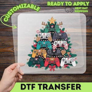 May include: A DTF transfer sheet featuring a Christmas tree design composed of various colorful video game controllers, decorated with string lights, holly berries, and a gold star topper, with a Santa face icon on each controller.