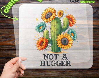 May include: A DTF transfer featuring a green cactus adorned with orange, yellow, and teal sunflowers. The text "NOT A HUGGER" is below the cactus. The transfer is labeled "CUSTOMIZABLE" and "READY TO APPLY".