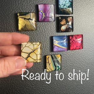 May include: Eight square-shaped magnets with abstract designs in various colors, including gold, purple, blue, red, and green. The magnets are arranged in a cluster on a gray surface. Ready to ship!