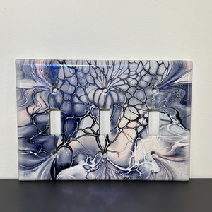 May include: A white light switch cover with a blue and white abstract design. The design features swirling patterns and a black outline.