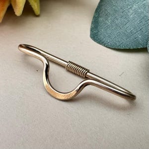 May include: A gold-toned metal body jewelry piece featuring a curved, U-shaped center section and a straight bar segment. The straight portion includes a textured, coiled wire detail. The overall design is smooth, polished, and metallic in appearance.