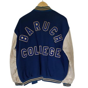May include: A navy blue varsity jacket with off-white sleeves. The back features the text BARUCH COLLEGE in large, arched, blue-outlined beige felt lettering. The collar, cuffs, and hem have striped navy, beige, and blue ribbed trim.