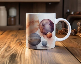 May include: White ceramic mug with a watercolor design of planets in shades of brown, purple, and gray. The planets are arranged in a cluster on a white background.