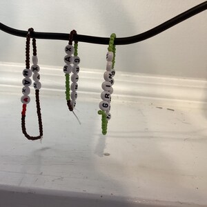 May include: Three beaded bracelets with white letter beads spelling out the names "MAX", "GRIN", and "GRAY". The bracelets are hanging from a black wire. The "MAX" bracelet has a red heart bead.