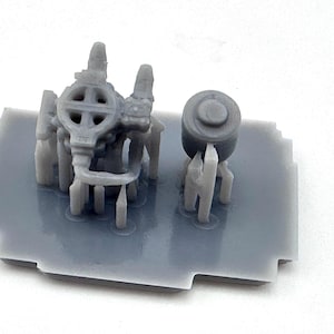 May include: A grey resin model kit featuring miniature components. The kit includes a cylindrical piece and a complex structure with a wheel-like design, all mounted on a rectangular base. The pieces are designed for model building.