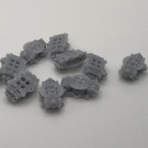 Puede incluir: Un grupo de diez piezas de modelo de coche de plástico gris, probablemente colectores de admisión, dispuestos en círculo sobre una superficie blanca.