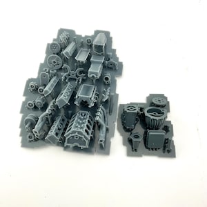 Peut inclure: Ensemble de pièces de moteur de modèle en plastique gris, comprenant des blocs, des cylindres et d'autres composants, disposées sur une plaque de plastique grise. Les pièces sont détaillées et semblent destinées à un véhicule miniature ou à un projet de modélisme.