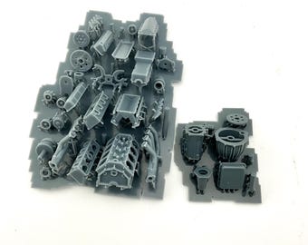 May include: A collection of gray plastic model engine parts, including blocks, cylinders, and other components, arranged on a gray plastic sheet. The parts are detailed and appear to be for a miniature vehicle or model project.