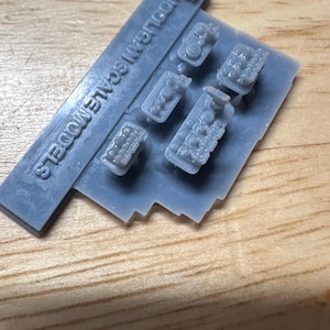 May include: A gray plastic sprue with several miniature engine models. The sprue includes the text "HOOLIGAN SCALE MODELS". A small, detached piece is also visible. The models are detailed and appear to be for hobby or model building.